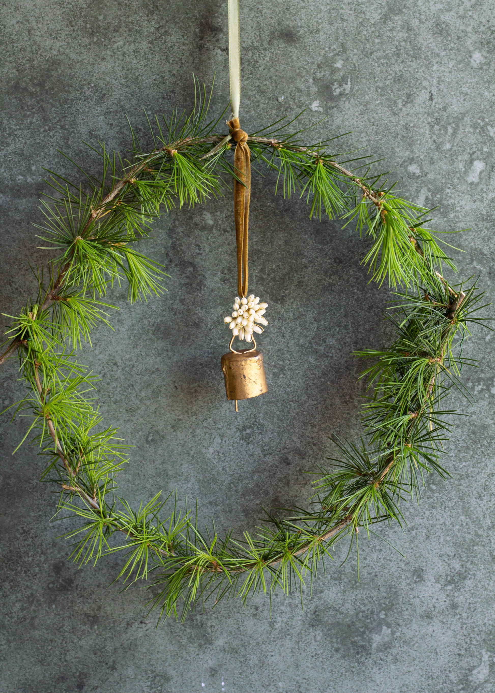 Wreath made of green branches with a gold bell and white flower on a gray background