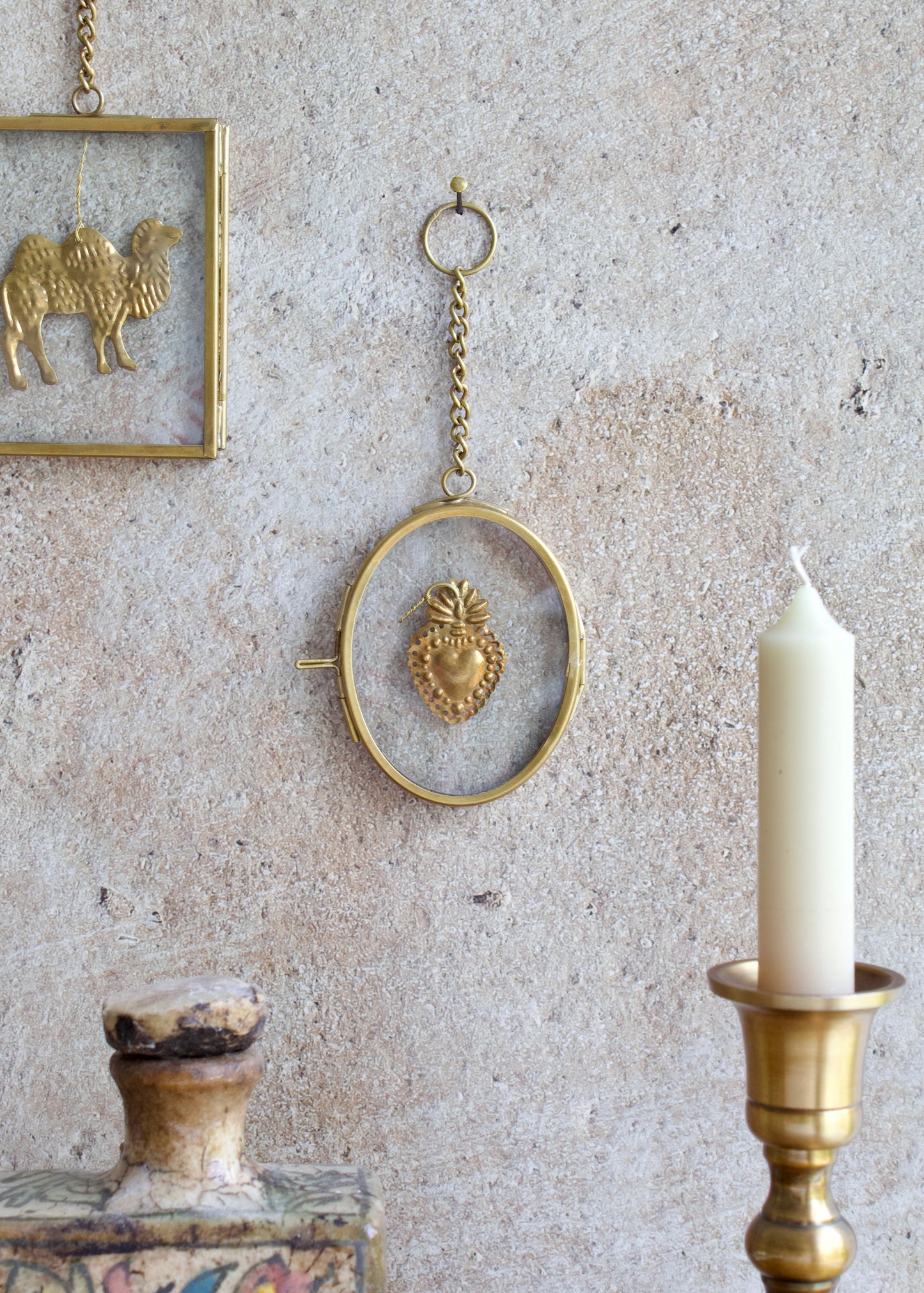 Decorative wall hanging with a heart design, candle, and framed animal art on a textured wall.
