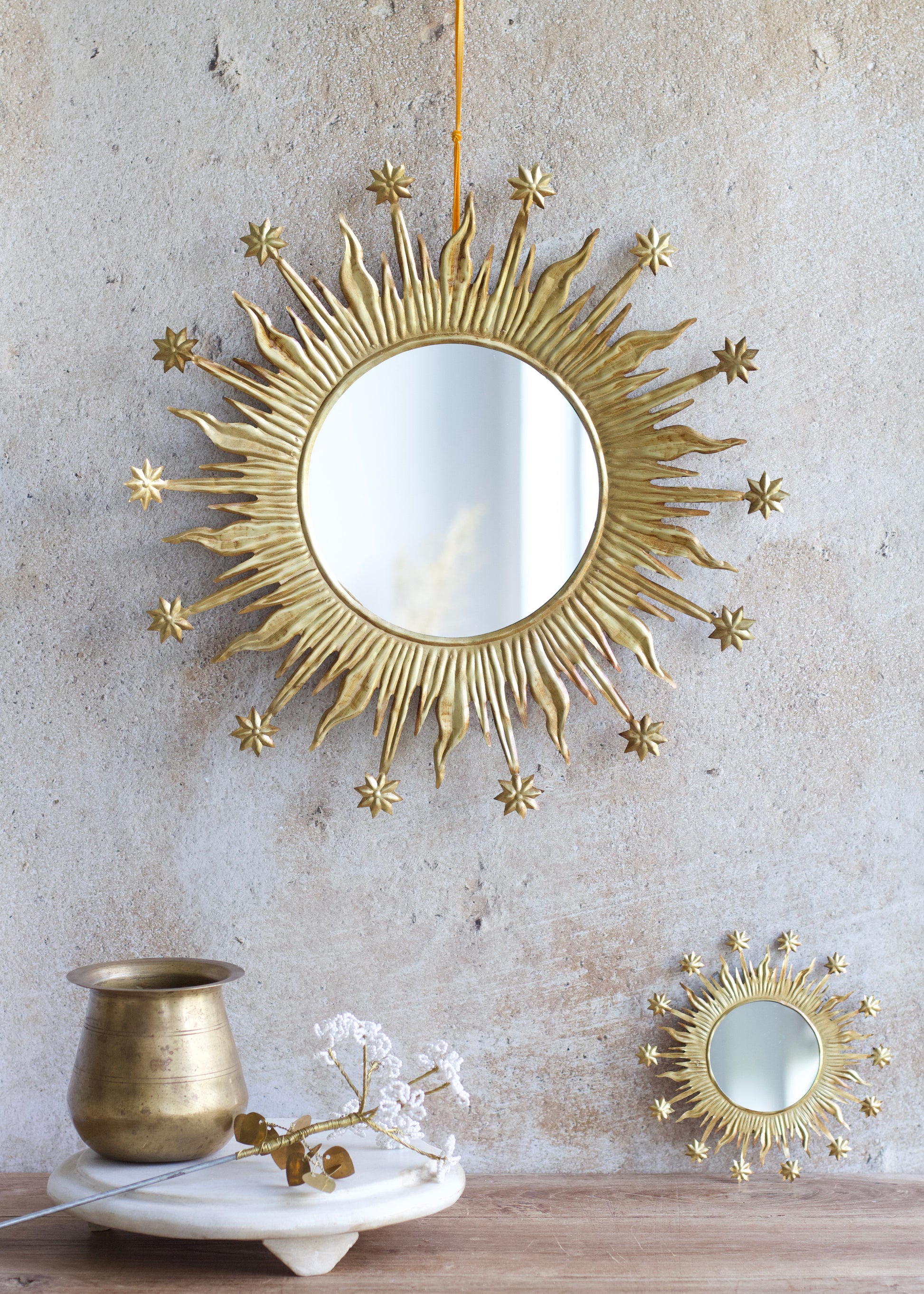 Decorative gold sunburst mirror on a textured wall with a small matching mirror below.