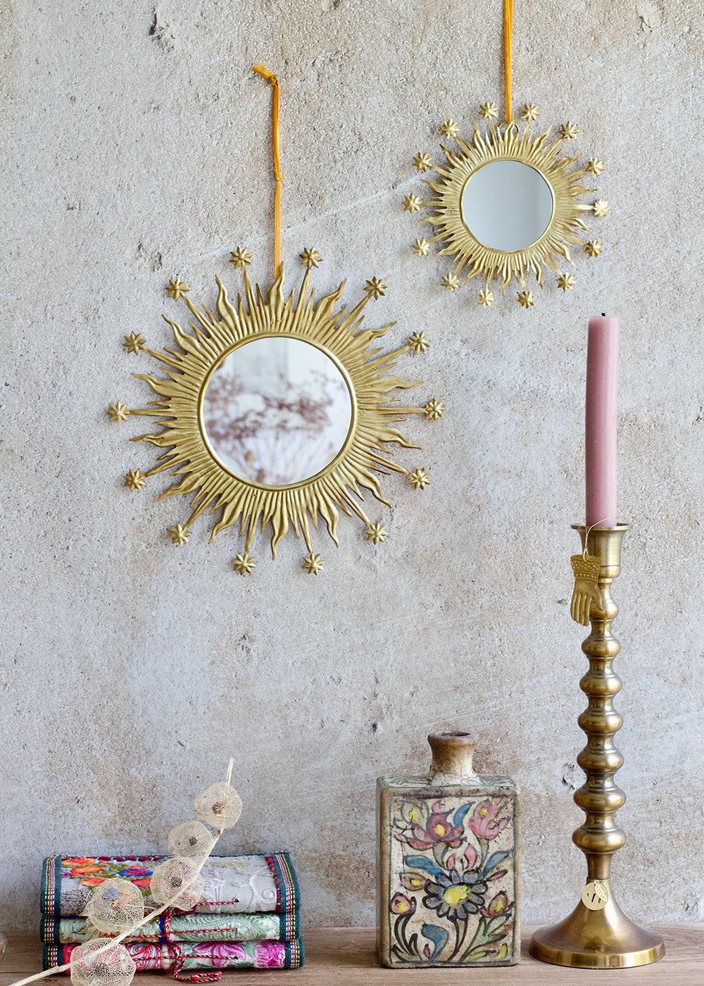 Decorative gold mirrors and candlestick with a pink candle on a textured wall.