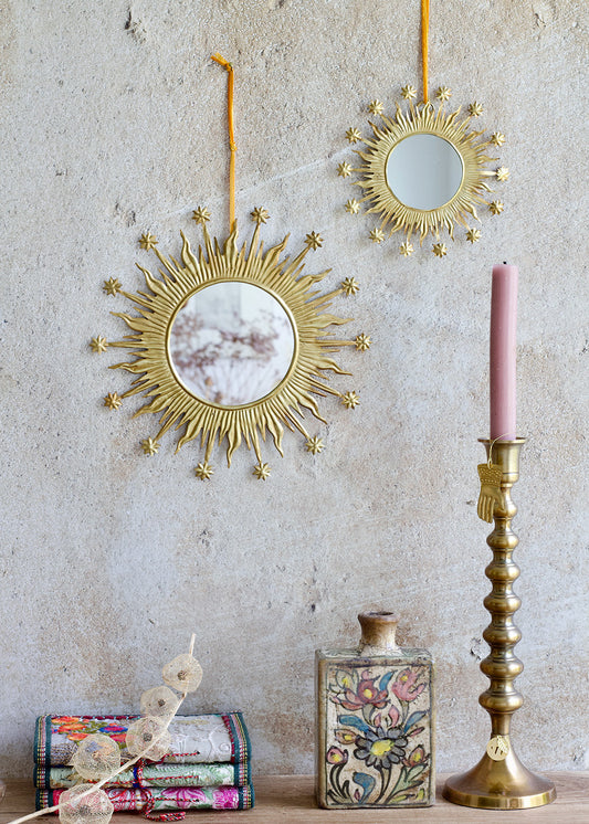 Decorative gold mirrors and candlestick with a pink candle on a textured wall.