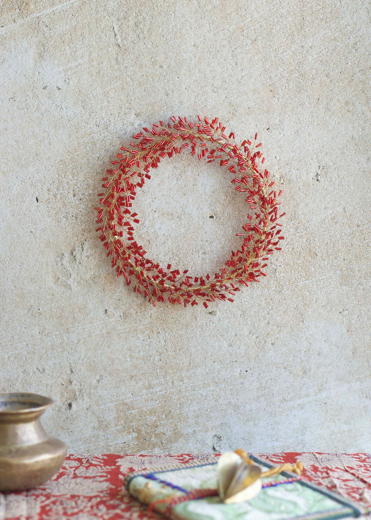 Decorative red wreath on a textured wall with a table and decorative items in the foreground.