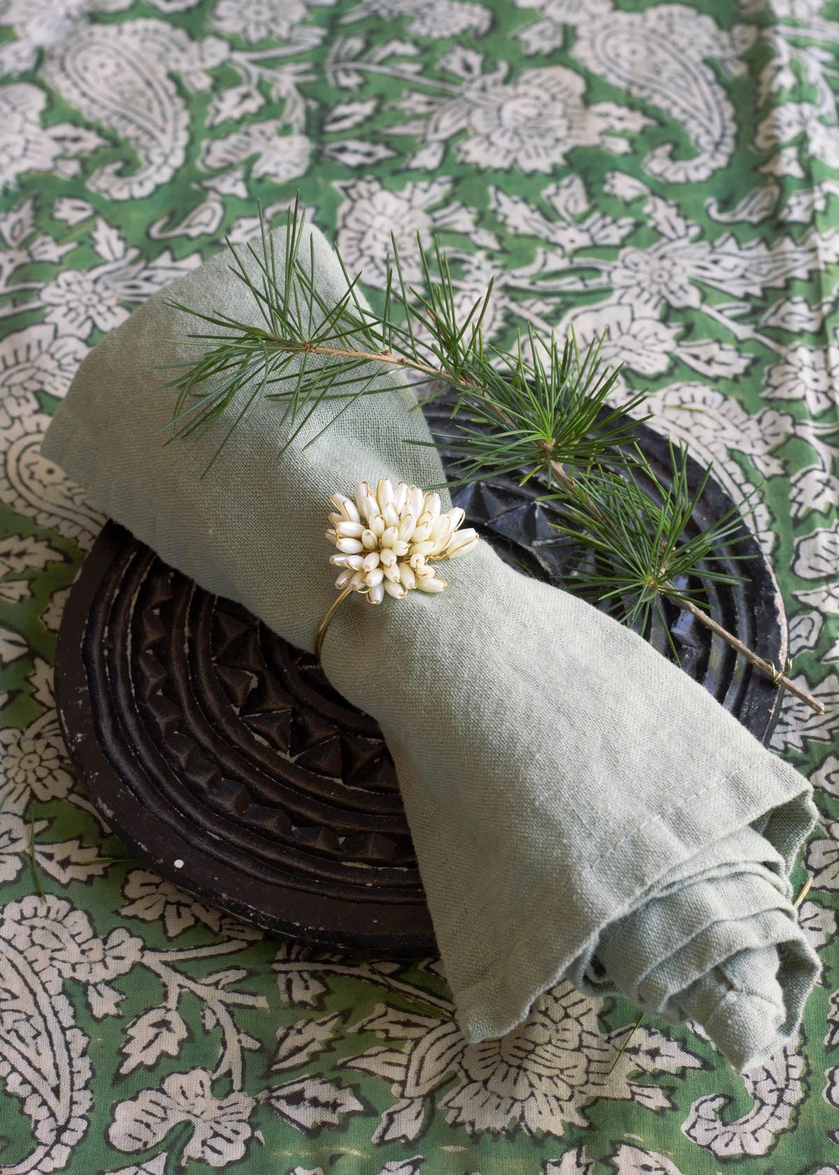 Green napkin with a decorative ring and pine branch on a patterned tablecloth