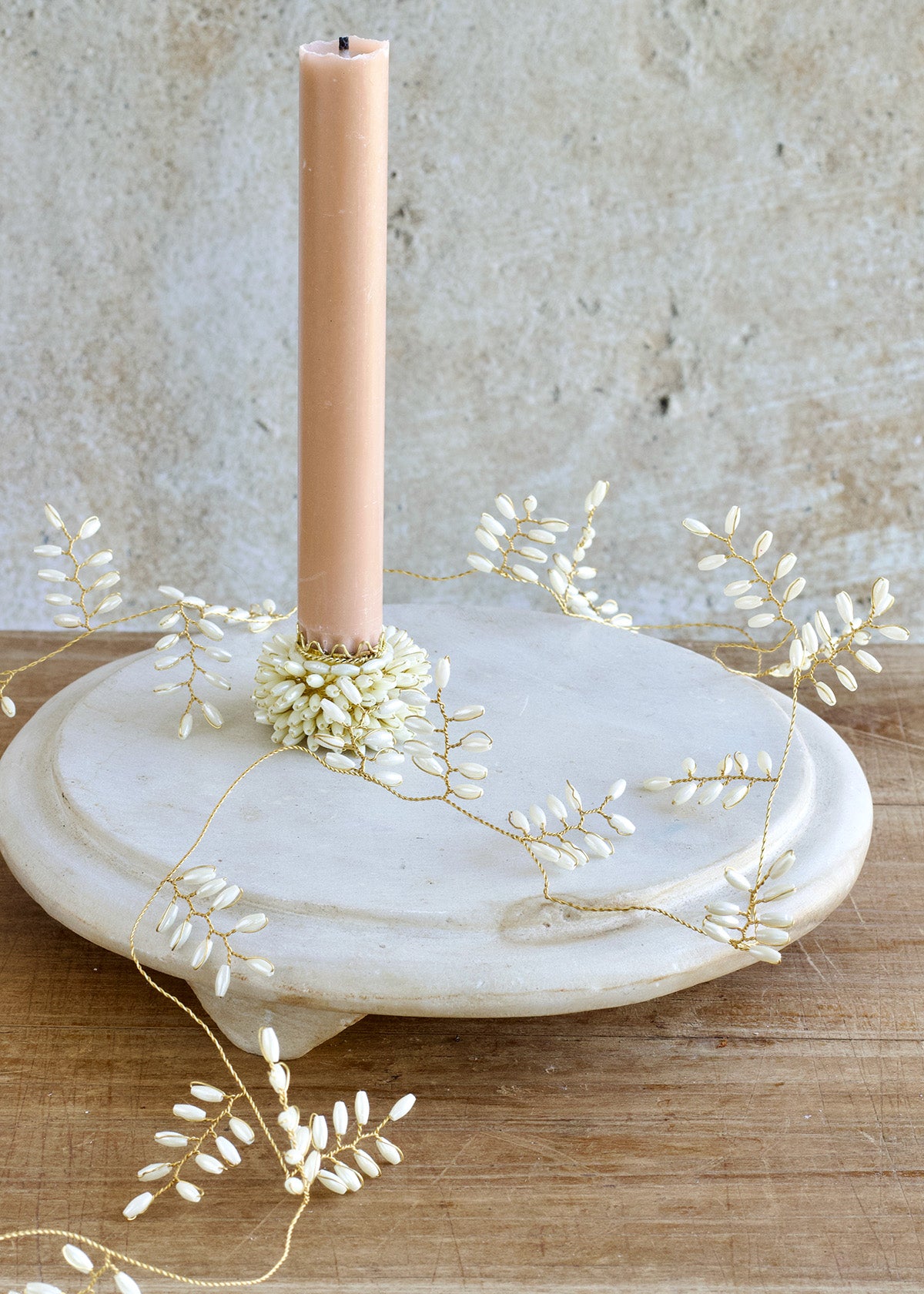 Candle on a marble holder with decorative branches against a textured wall.