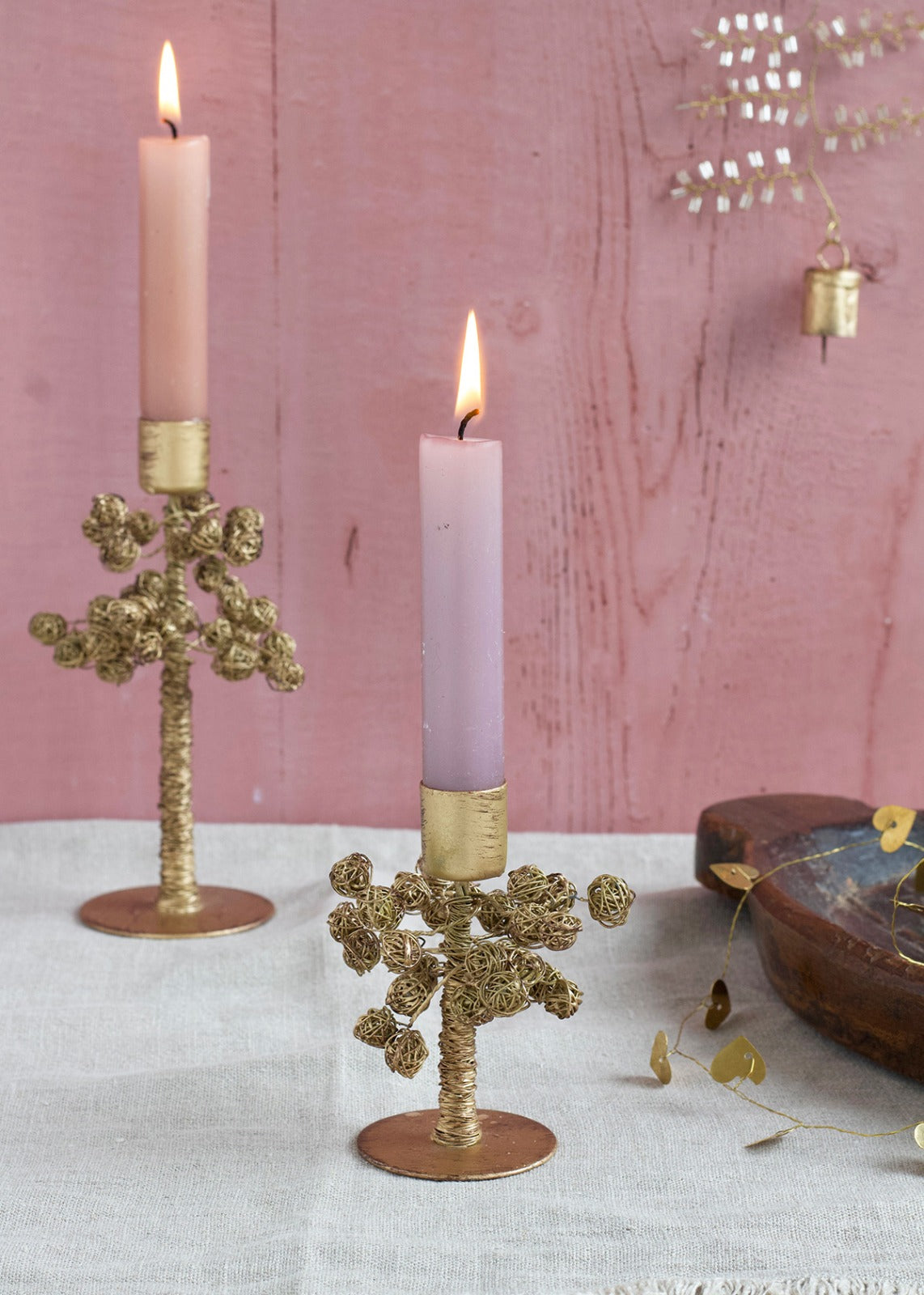 Two candle holders with a copper-coloured metal design, each holding a pink candle, placed on a table with decorative items in the background.