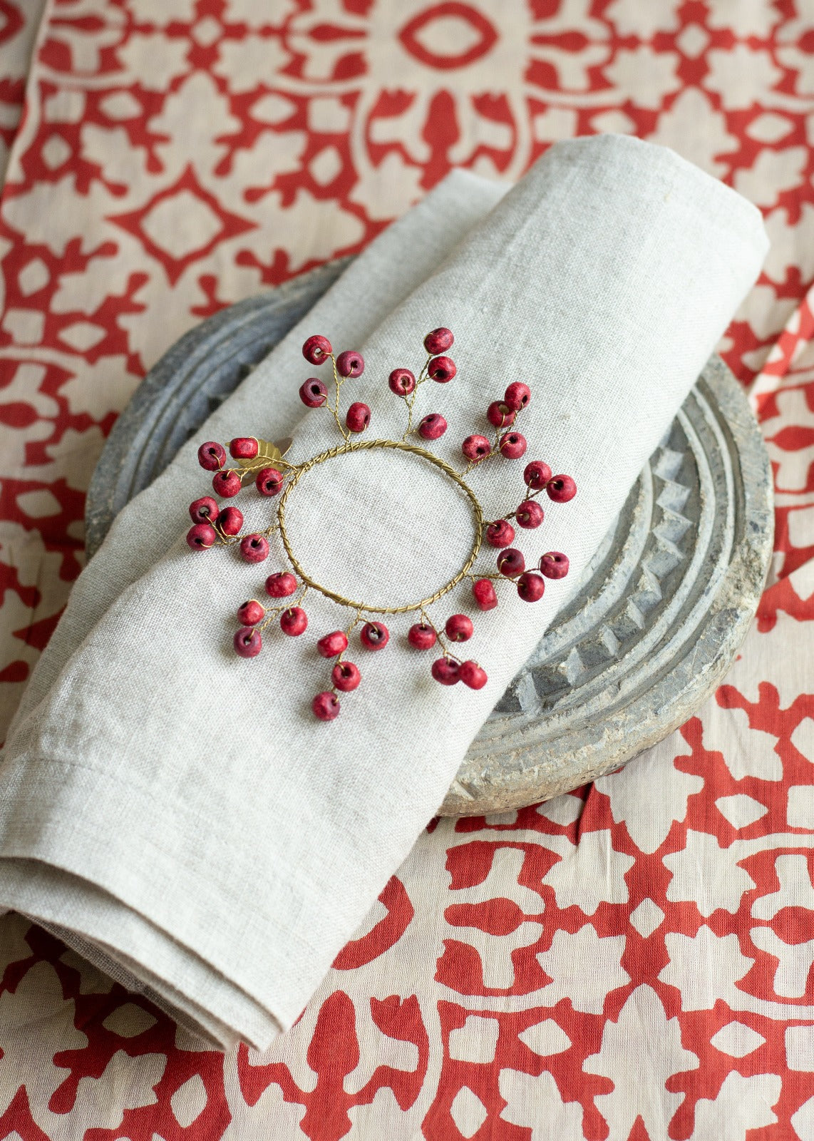 A wooden napkin ring with red accents displayed on a white napkin, placed on a table with a patterned tablecloth.