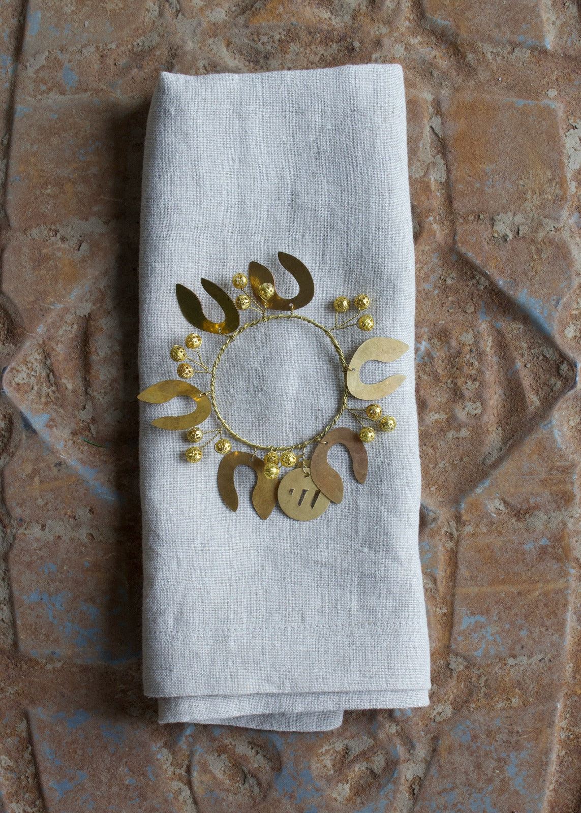 A white napkin with a gold-colored mistletoe pattern napkin ring adorned with small gold beads.