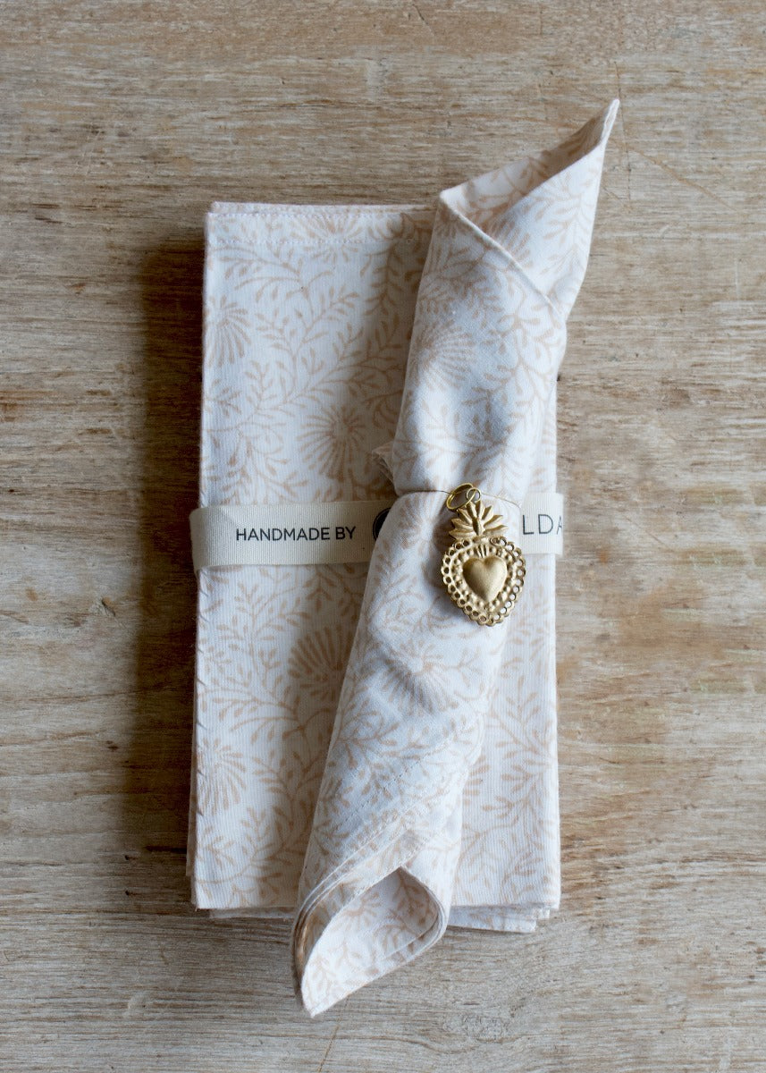 A handmade brass ornament in the shape of a sacred heart, displayed on a wooden surface, with a decorative patterned fabric.
