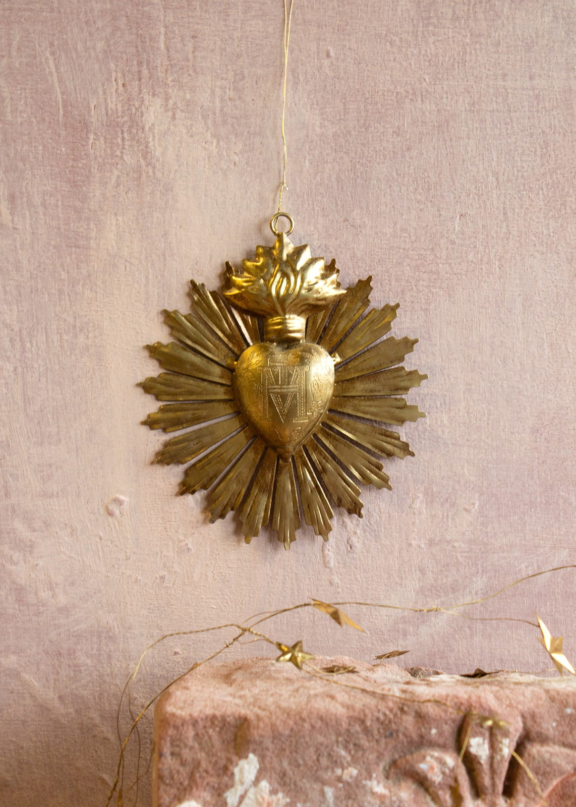A collection of gold-colored brass mirrors with a distinctive radiant heart design, hanging against a pink background with stars.