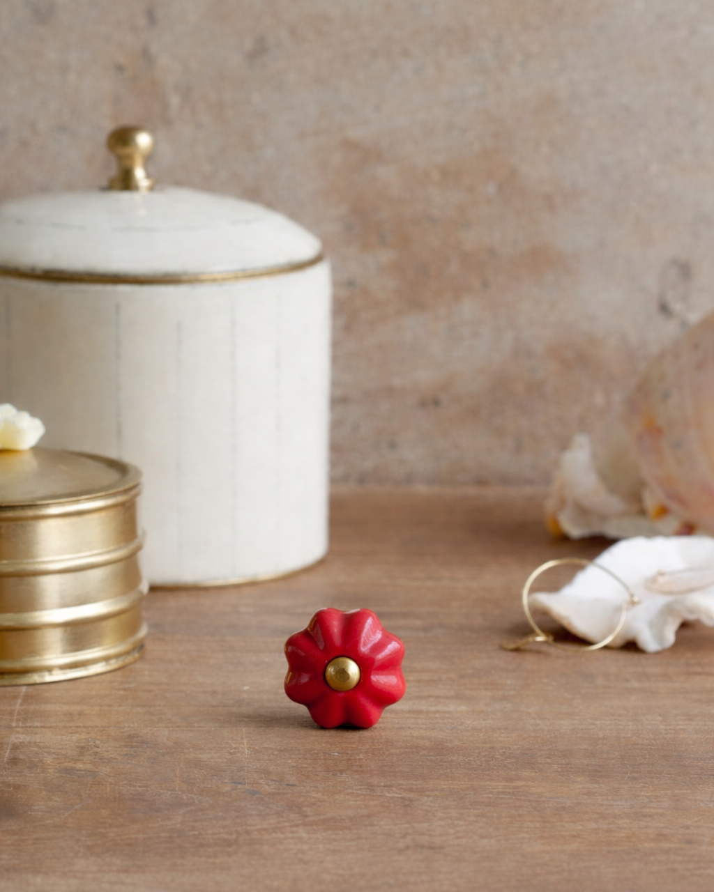 Red decorative knob on a wooden surface with a white container and gold accents in the background.