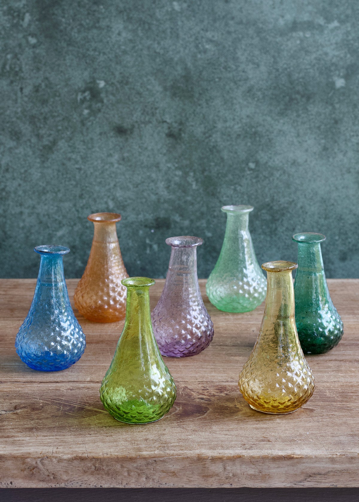 Set of colorful glass vases on a wooden surface with a textured gray background