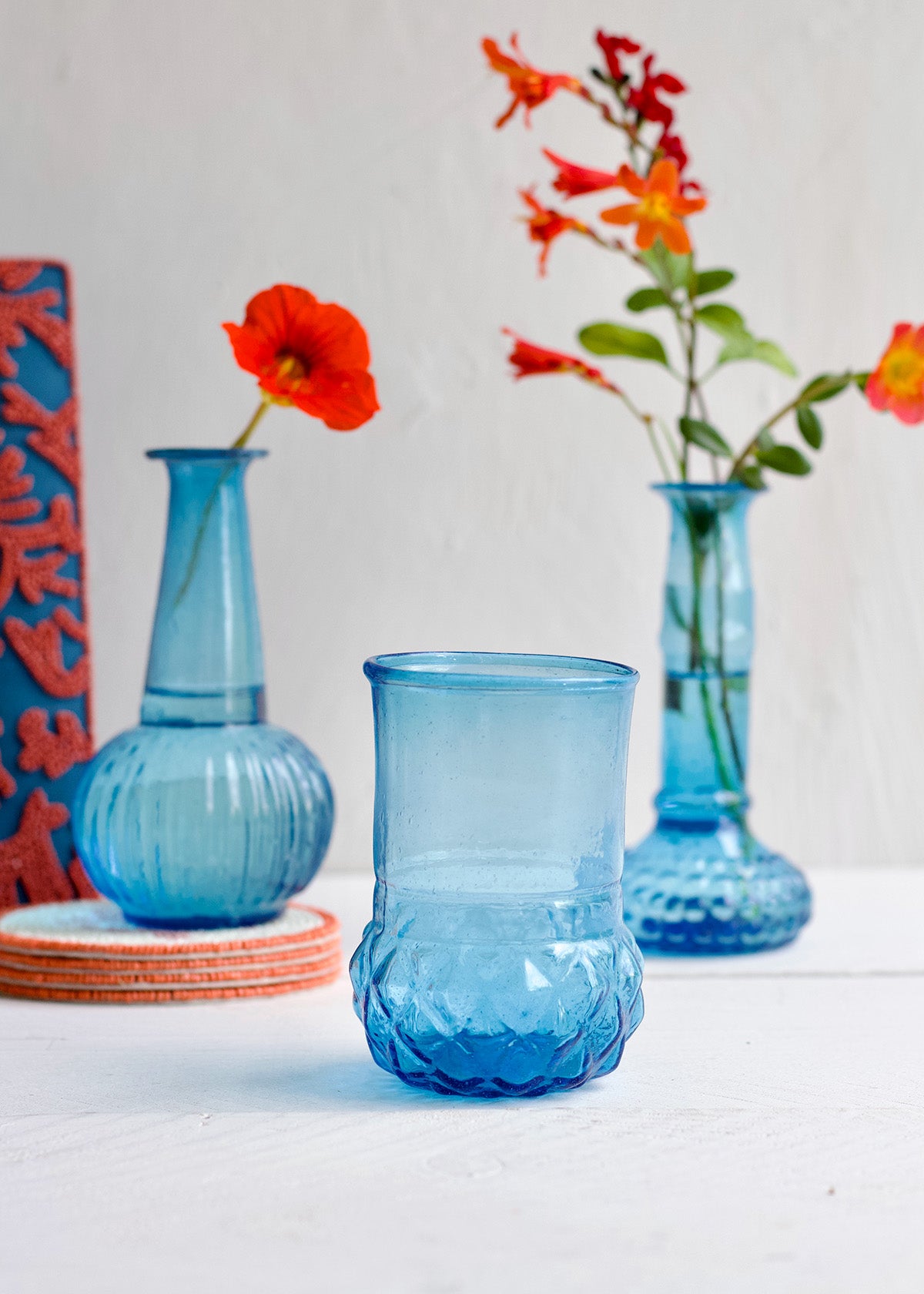 Blue glass vase with textured design on a white surface, surrounded by other decorative items.