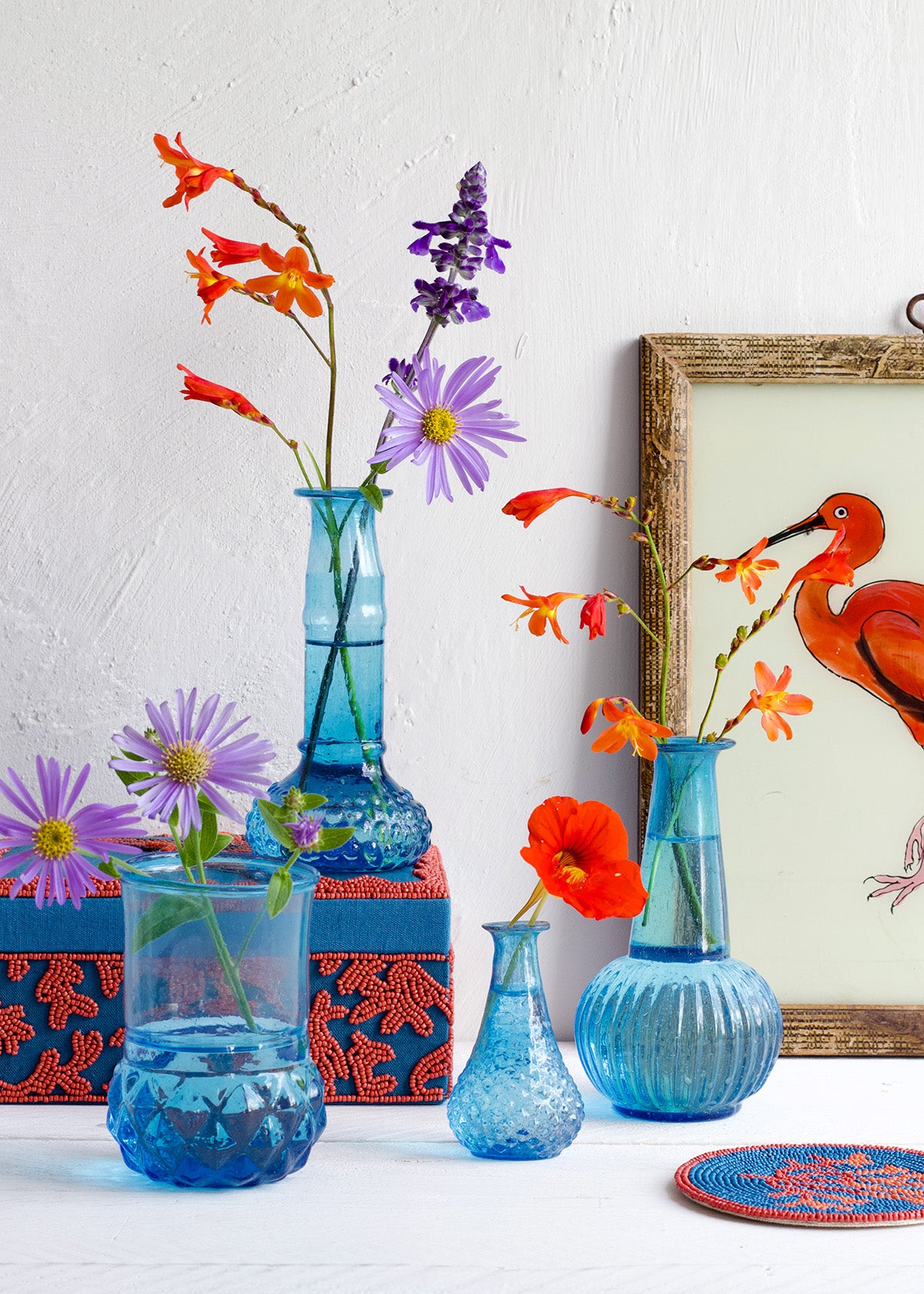Decorative blue vases with flowers on a white surface, featuring a framed artwork in the background.
