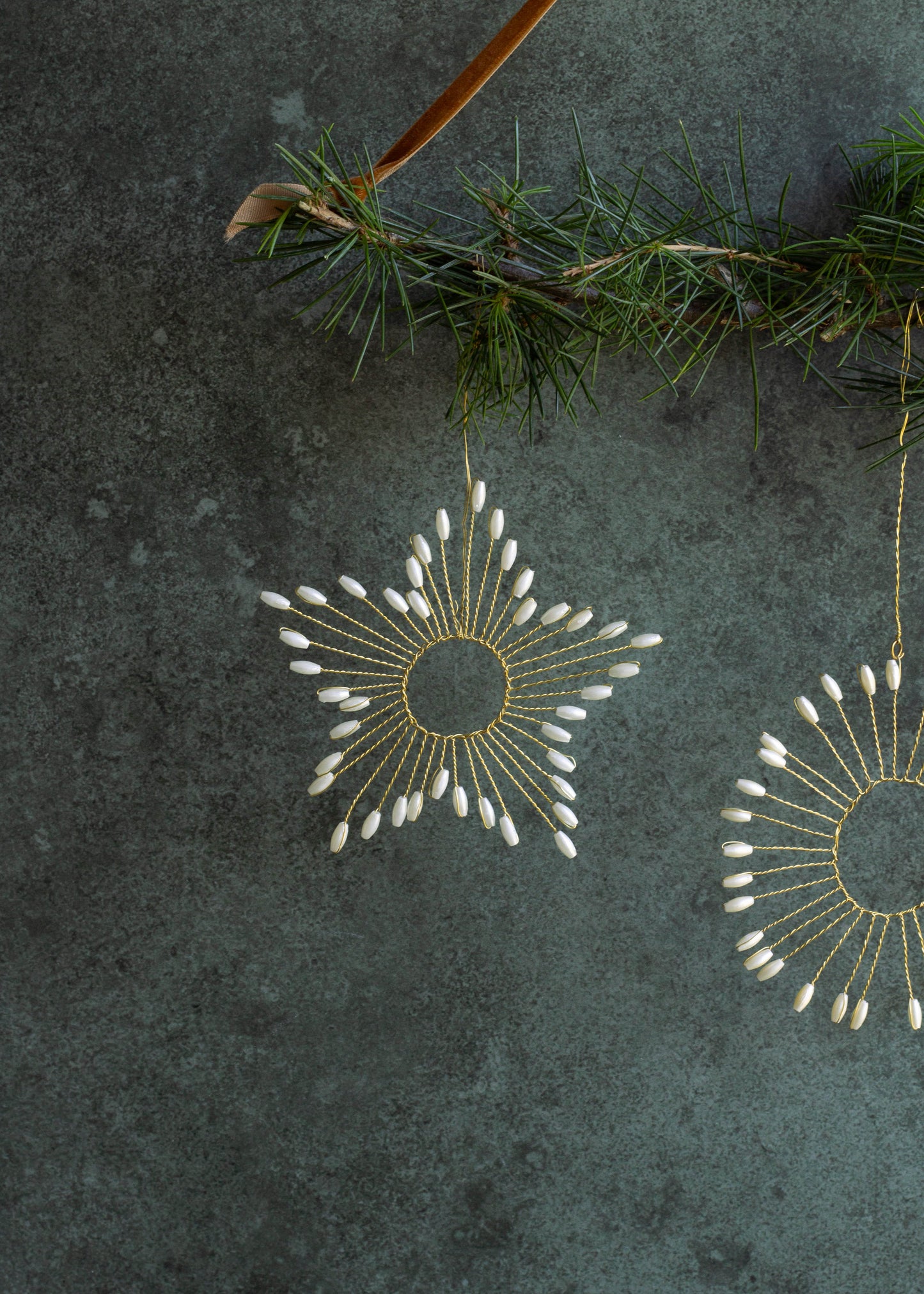 Decorative gold and white ornaments hanging on a branch against a dark textured background