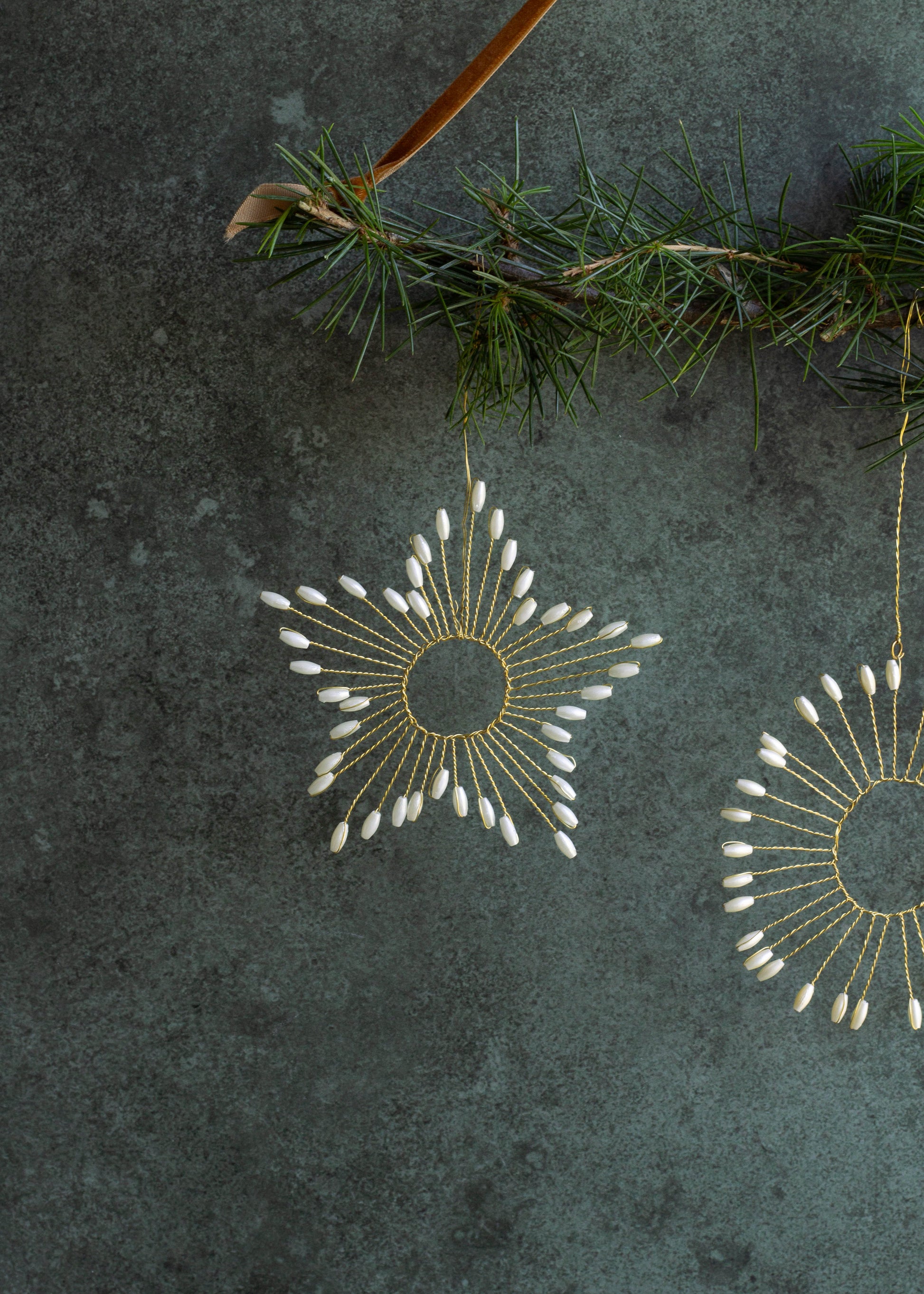 Decorative gold and white ornaments hanging on a branch against a dark textured background