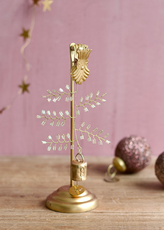 Gold decorative tree with crystal-like branches on a wooden surface against a pink background