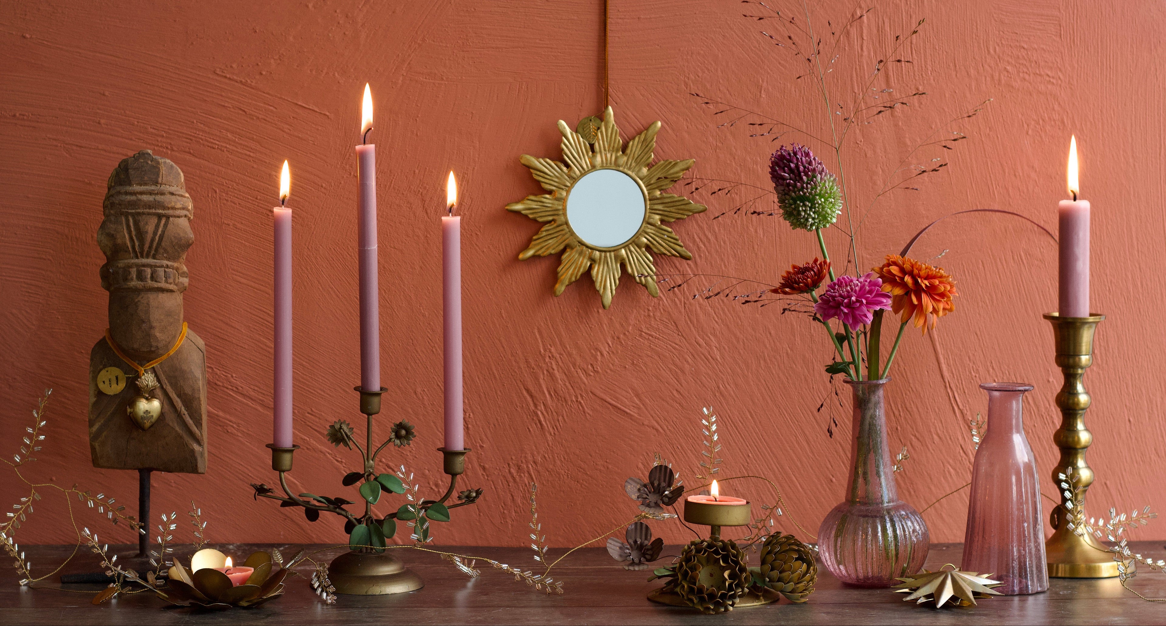 Decorative setup with candles, flowers, and a mirror on a wooden surface against a pink wall.