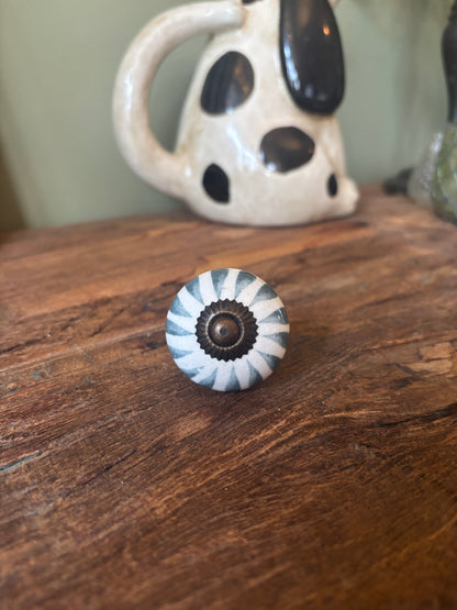Decorative cabinet knob on a wooden surface with a ceramic item in the background