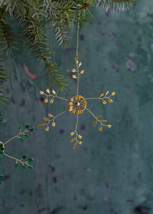 Decorative gold ornament hanging from a branch with a textured green background