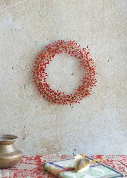 Decorative red wreath on a textured wall with a table and decorative items in the foreground.