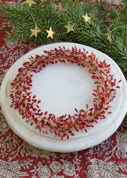 Decorative plate with red and gold wreath design on a patterned surface with greenery and stars.