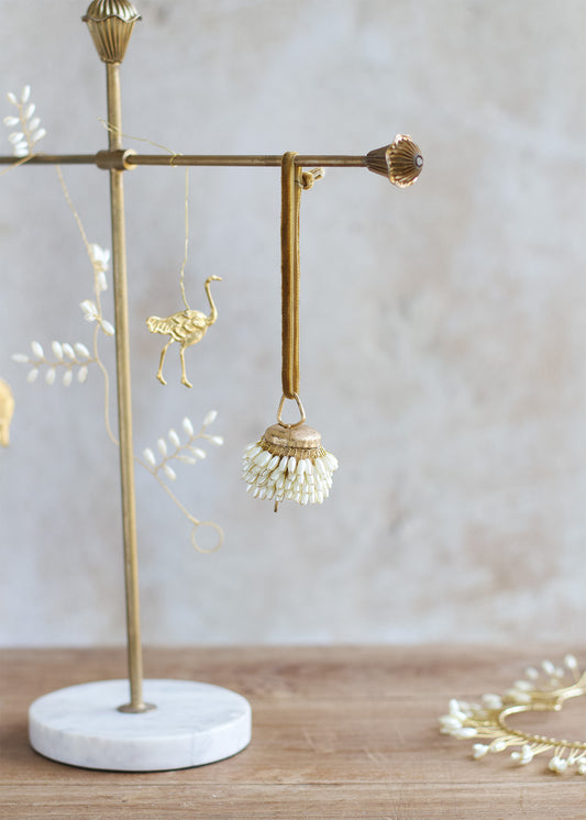 Gold earring stand with a decorative earring on a marble base against a light background