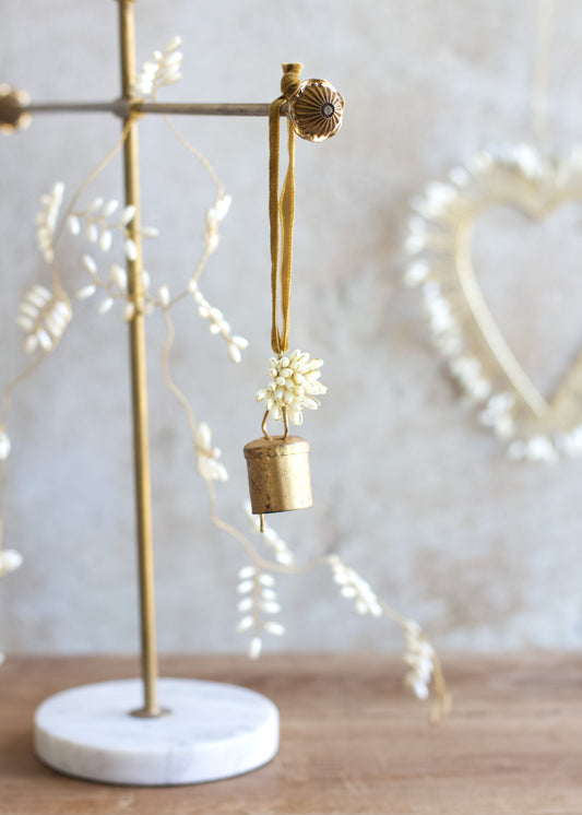 Decorative brass bell with floral elements on a marble stand against a neutral background