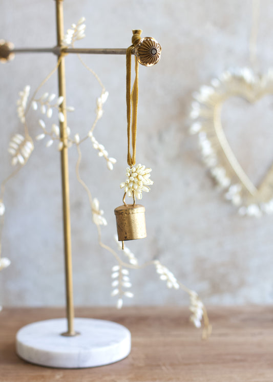 Decorative brass bell with floral elements on a marble stand against a neutral background