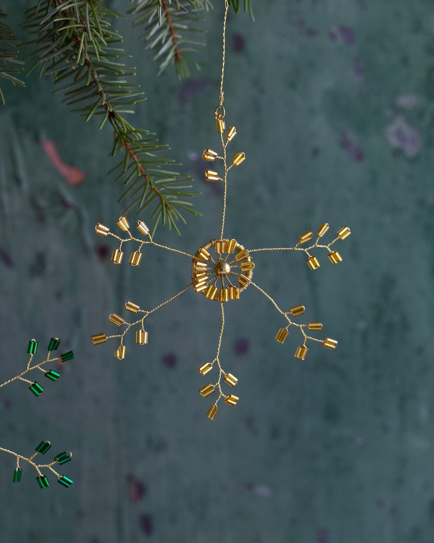 Decorative gold ornament hanging from a branch with a textured green background
