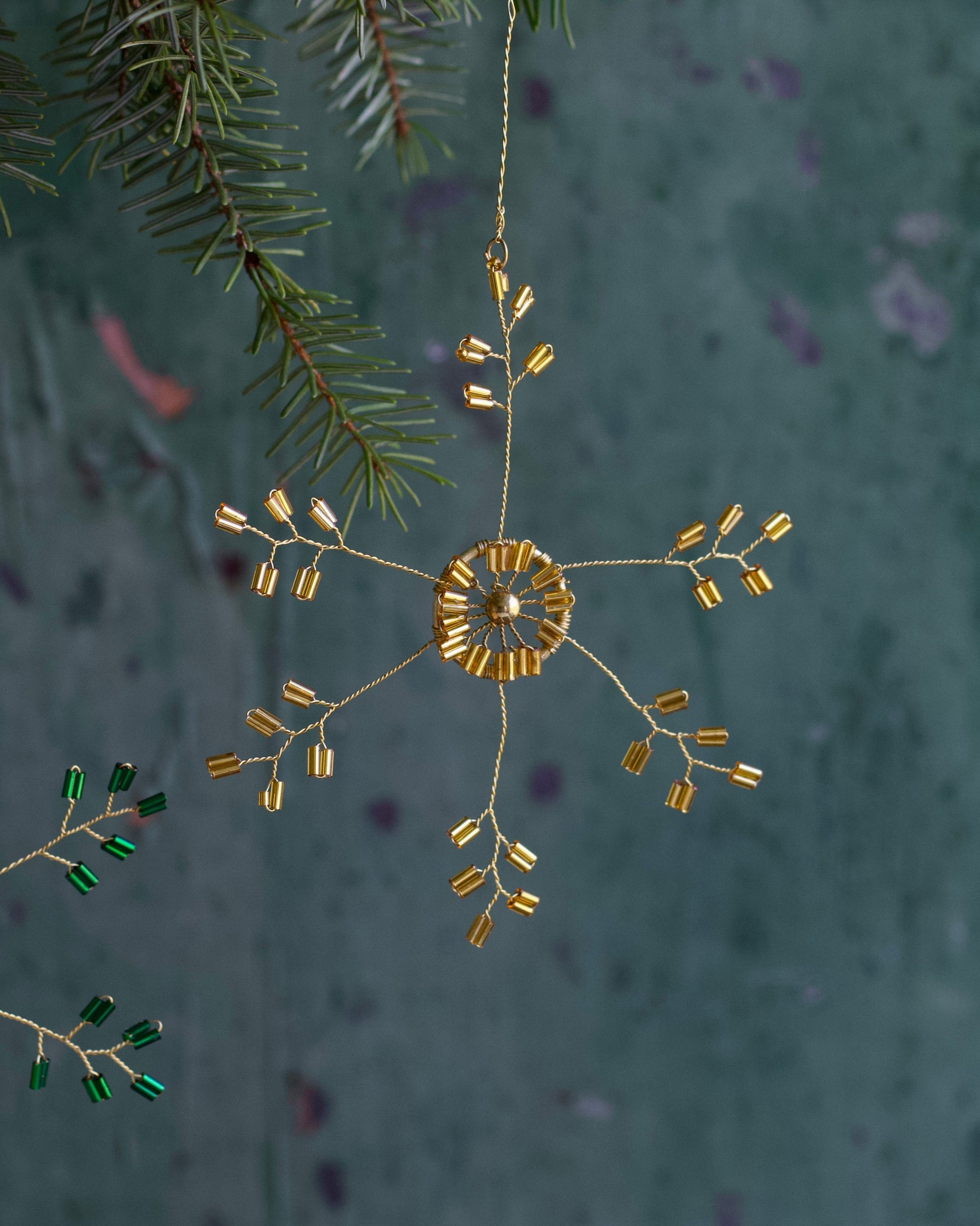 Decorative gold ornament hanging from a branch with a textured green background