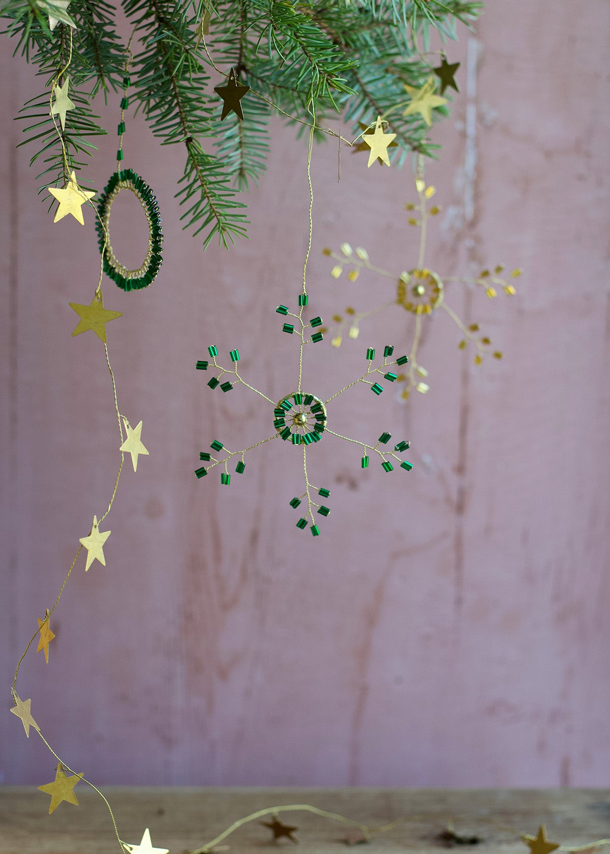 Decorative string with stars and green beads hanging against a pink background