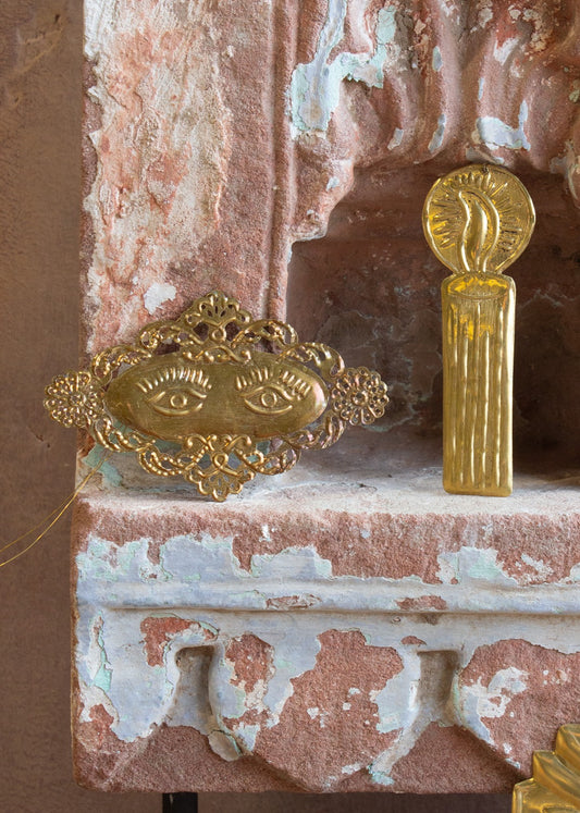 A decorative brass pendant featuring two eyes, placed on a textured surface with a reflective gold finish.