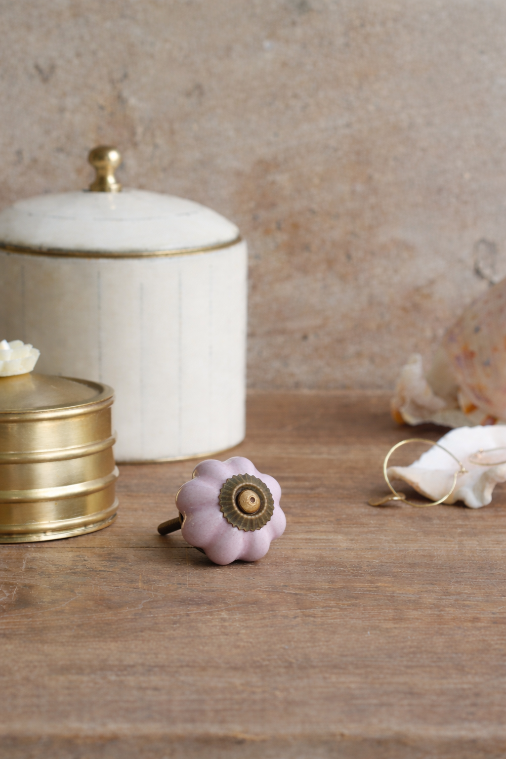 Pink ceramic knob with gold center on a wooden surface, with decorative jars in the background.