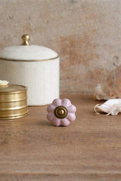 Pink floral knop with gold center on a wooden surface, with decorative jars in the background.