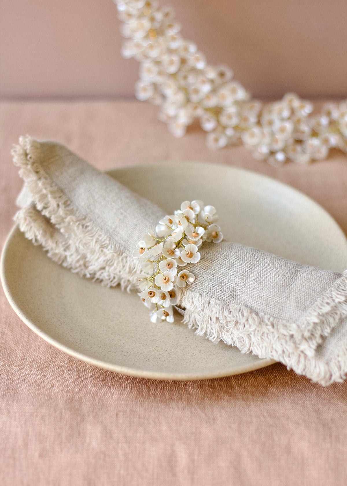 Napkin folded on a plate with a decorative napkin ring featuring small white flowers on a pink background.