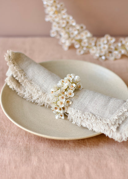 Napkin folded on a plate with a decorative napkin ring featuring small white flowers on a pink background.