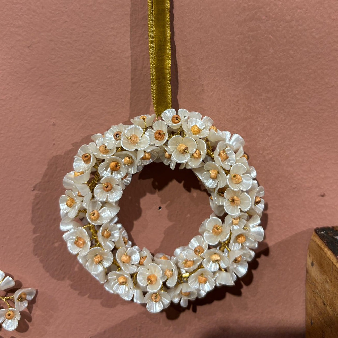 Decorative wreath with white flowers and gold accents on a pink background