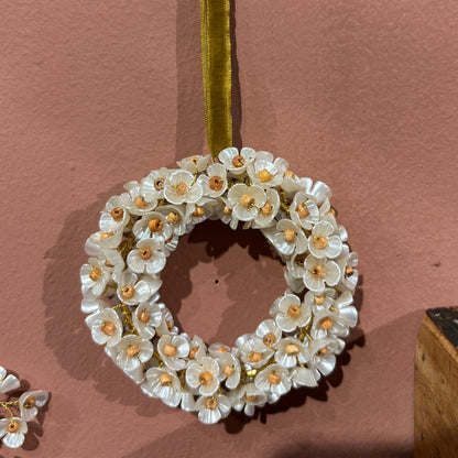 Decorative wreath with white flowers and gold accents on a pink background