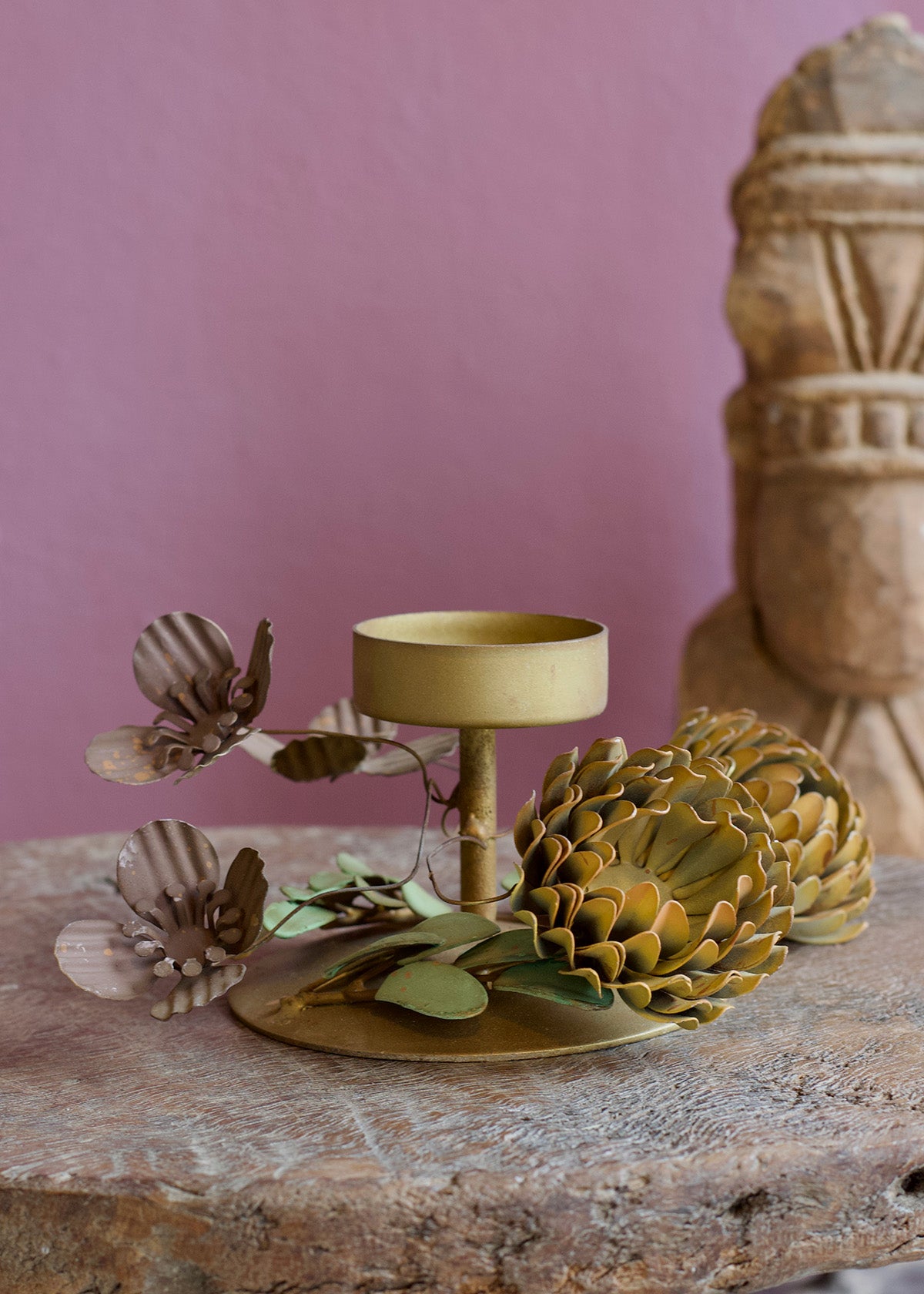 Decorative candle holder with floral design on a stone surface against a pink wall.