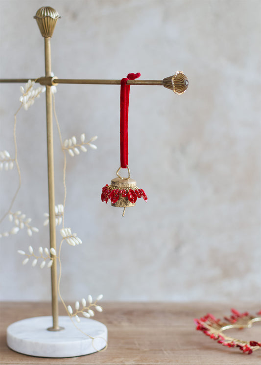 Decorative bell with red beads hanging on a gold stand with a white base.