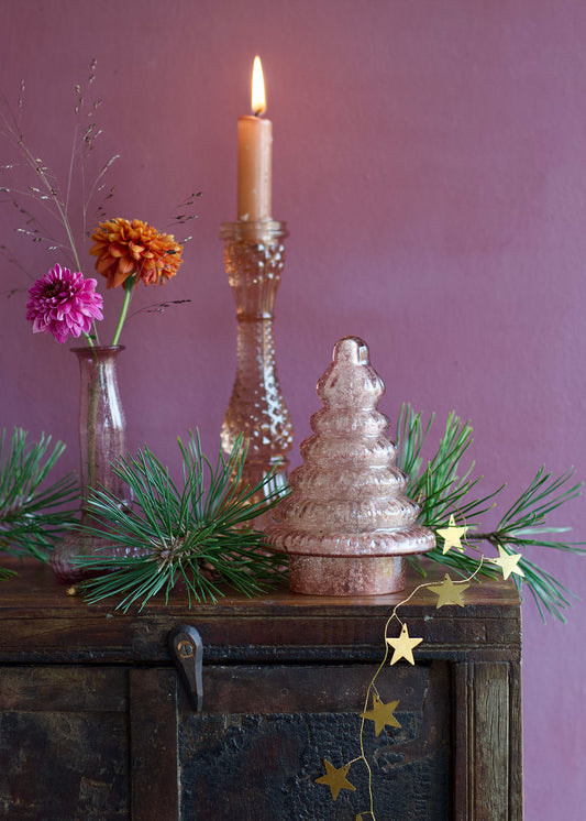 Decorative setup with candles, flowers, and greenery on a wooden surface against a purple wall.
