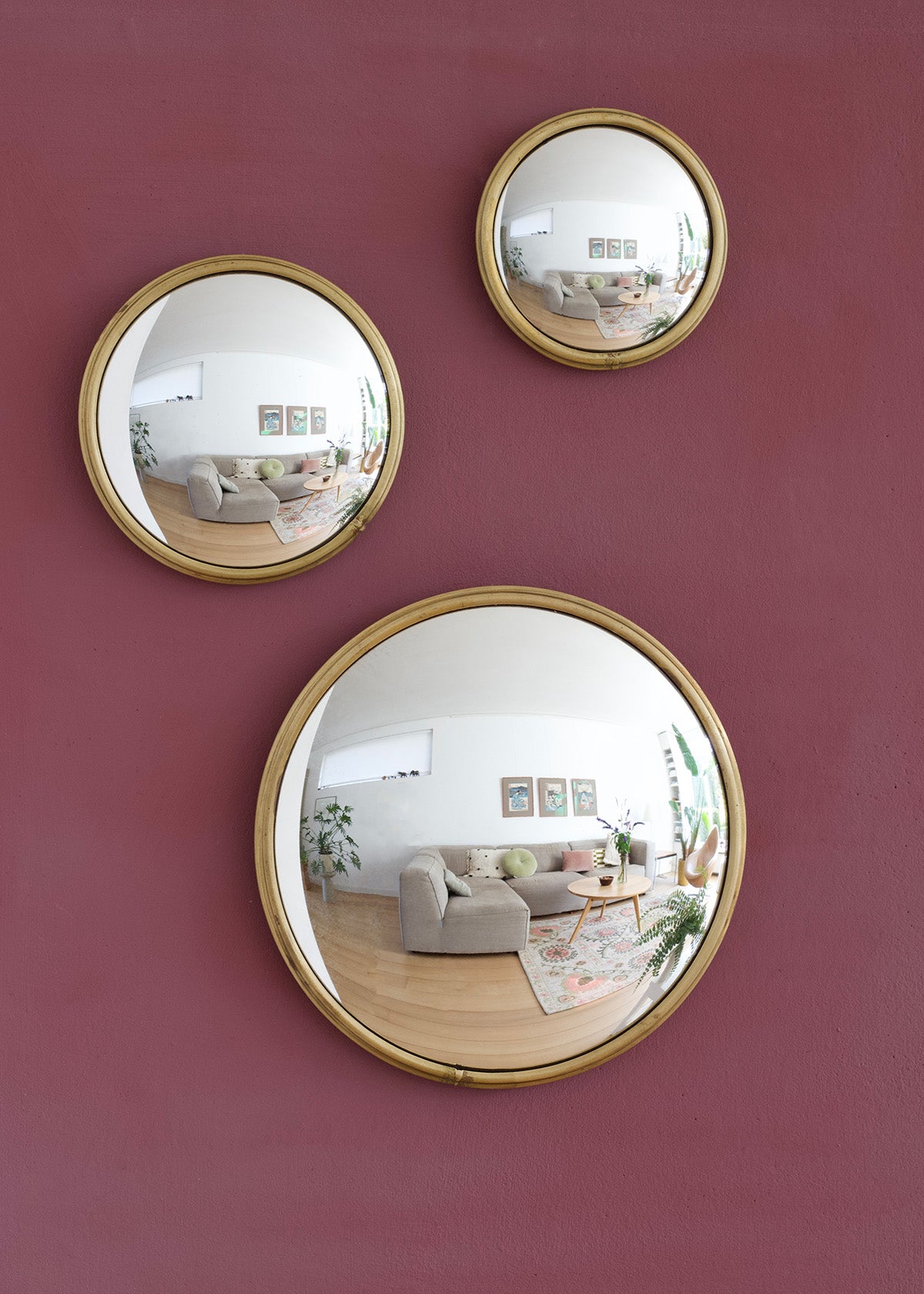 Three round gold-framed mirrors on a pink wall reflecting a living room.