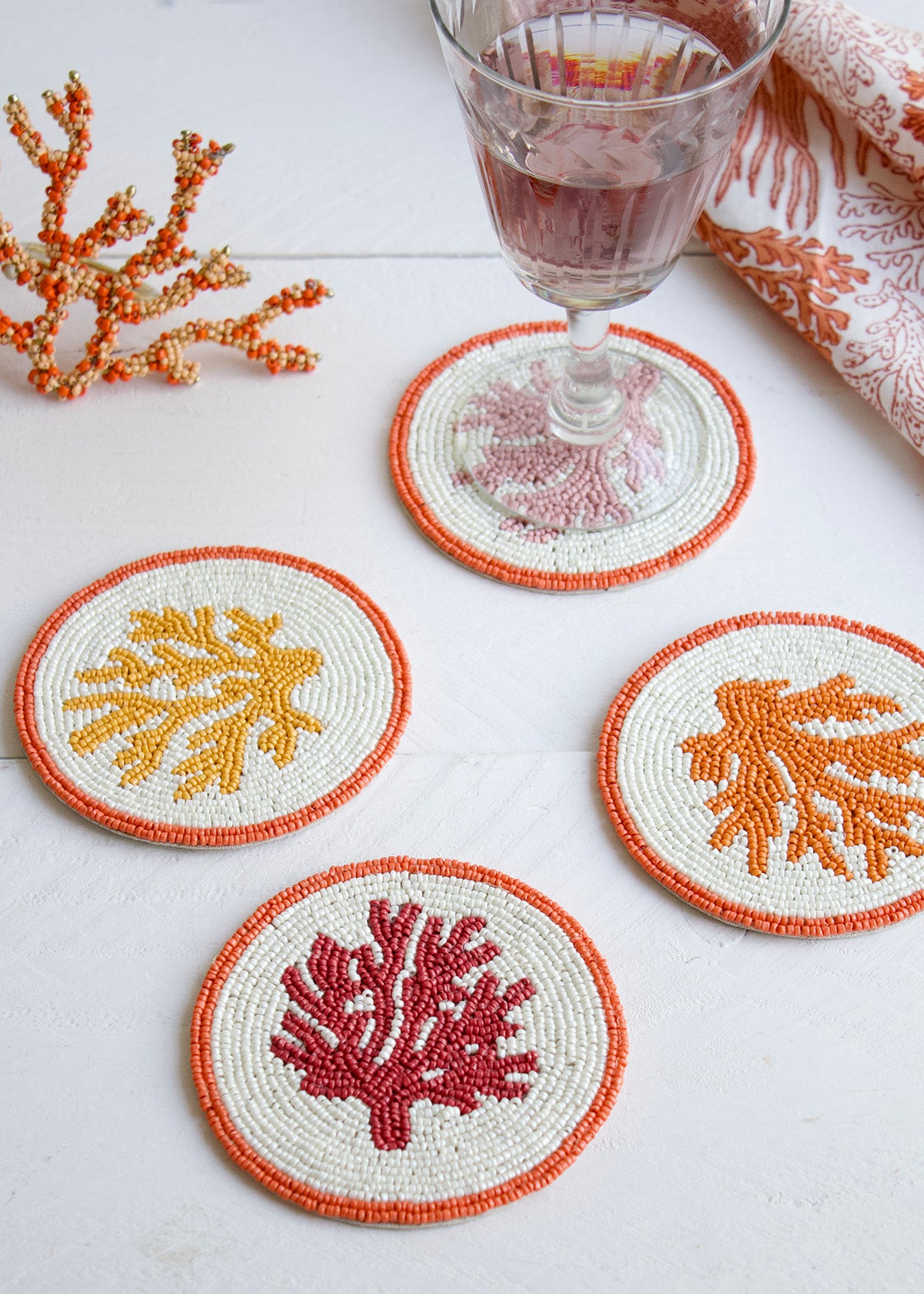 Set of four coral-themed coasters with a glass of red wine on a white surface.