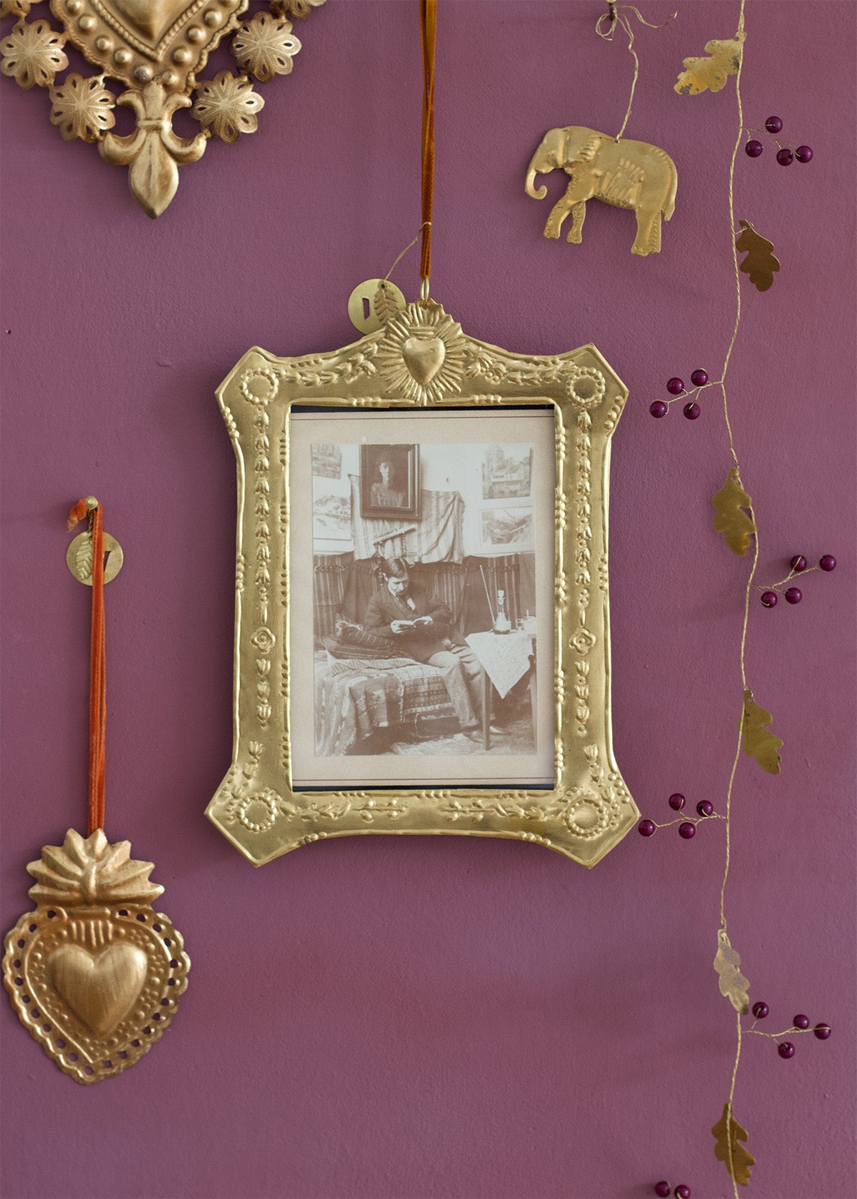 Decorative gold frame with a vintage photo on a purple wall with hanging ornaments.