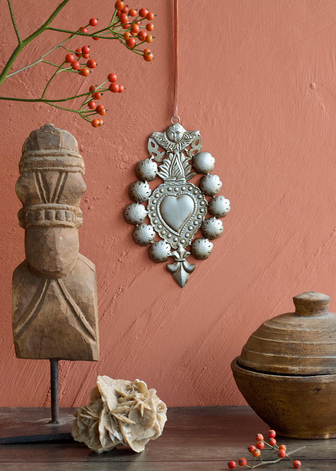 Decorative wall hanging with a heart design, wooden sculpture, and ceramic pot against a pink wall.