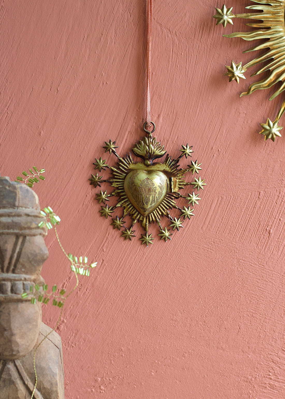 Decorative brass heart with starburst design on a pink wall