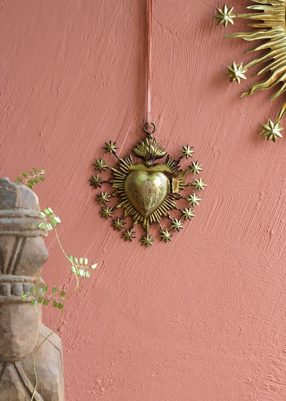Decorative brass heart with starburst design on a pink wall