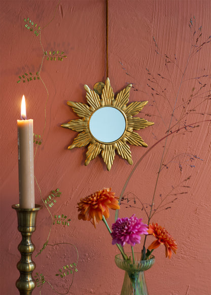 Decorative gold sunburst mirror on a pink wall with a candle and flowers.