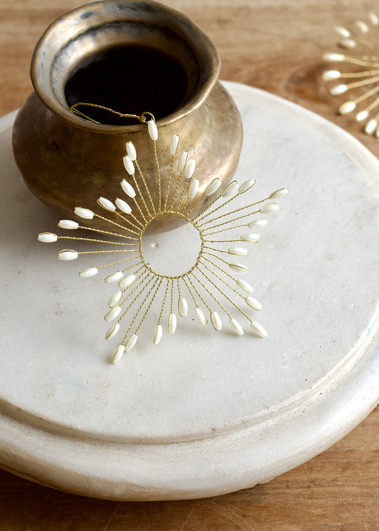 Decorative earring on a marble surface with a small pot of dark liquid.