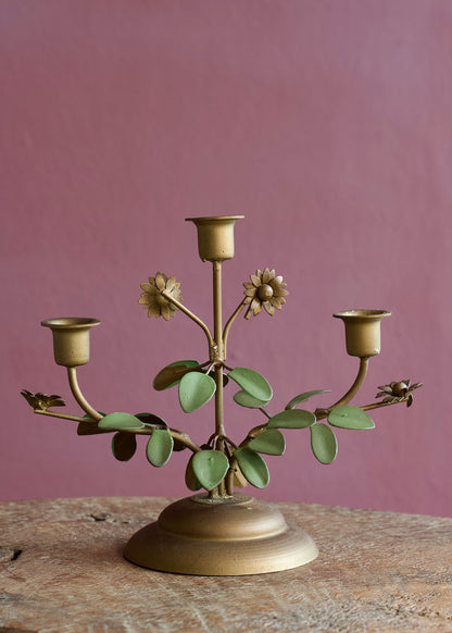 Decorative brass candelabra with floral and leaf designs on a wooden surface against a pinkish-purple wall.